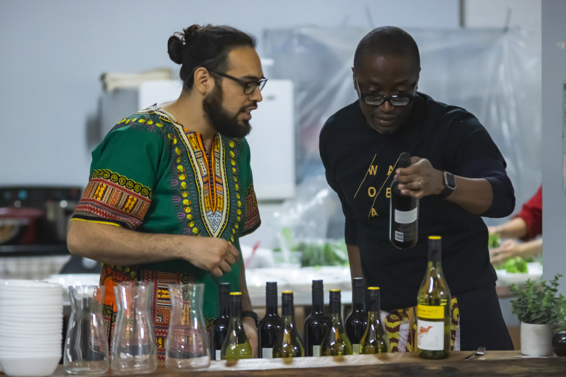 two cooks in a kitchen with wine bottles